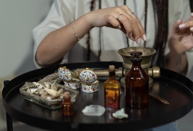 Hands crafting handmade vintage decor with glass bottles, natural crystals and botanical materials on dark tray